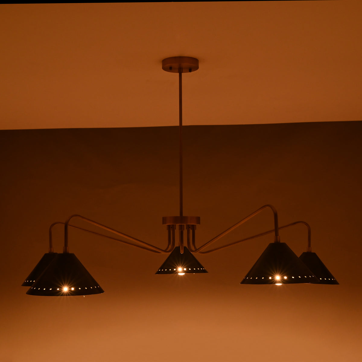 Soft warm light photo of 5-light brass cone chandelier with slender modern brass arms and matte-black cone shades.