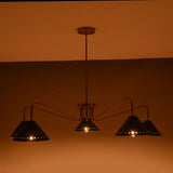 Soft warm light photo of 5-light brass cone chandelier with slender modern brass arms and matte-black cone shades.
