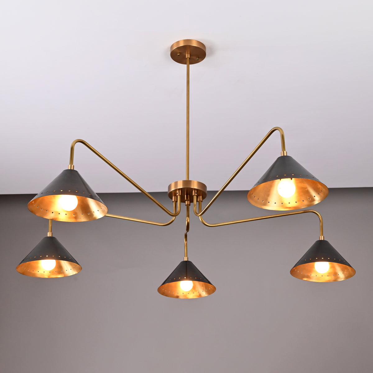 Angled view of modern 5-light brass cone chandelier with warm illumination and sleek sculptural brass frame.