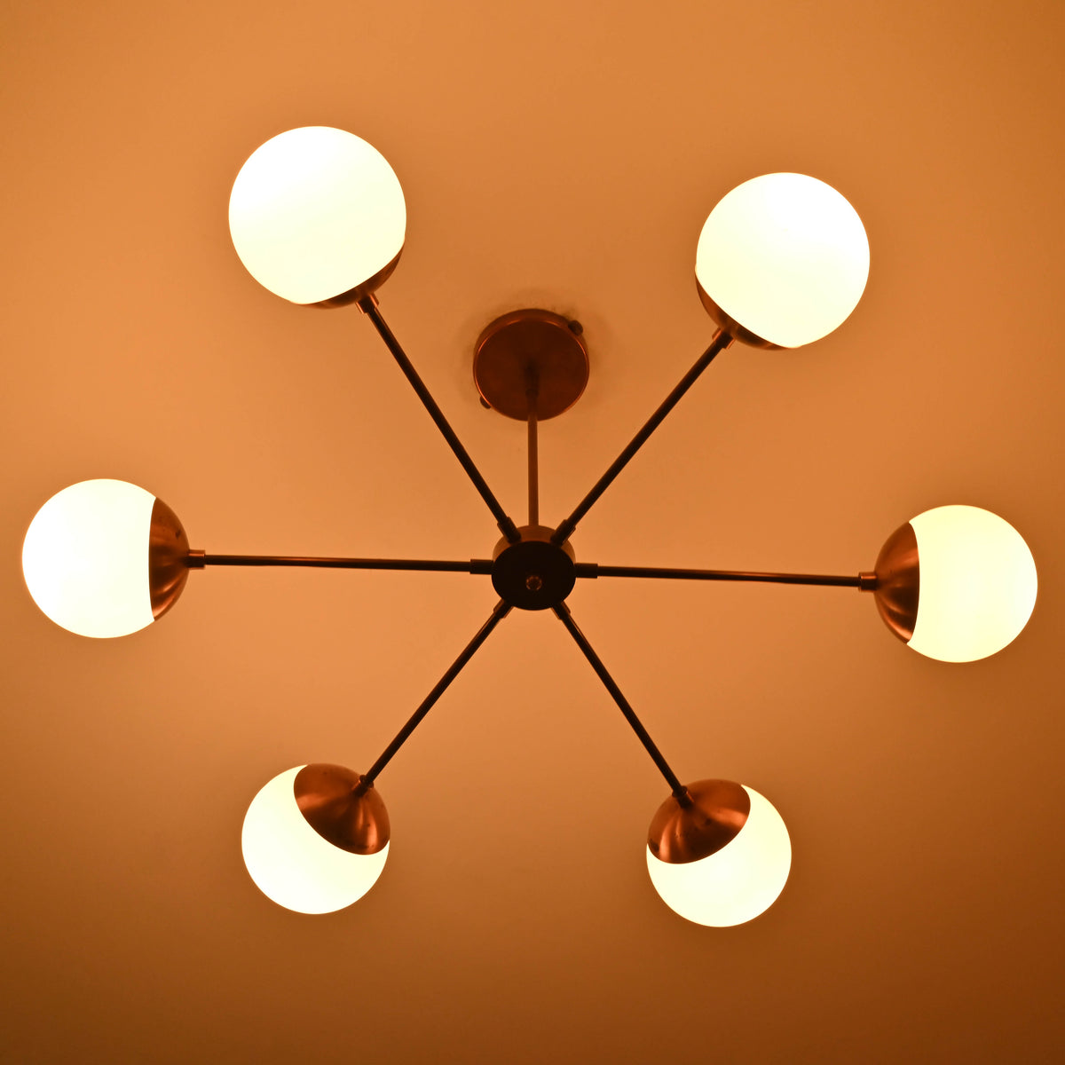 Illuminated 6 light glass globe brass chandelier highlighting brushed brass arms and soft diffused light