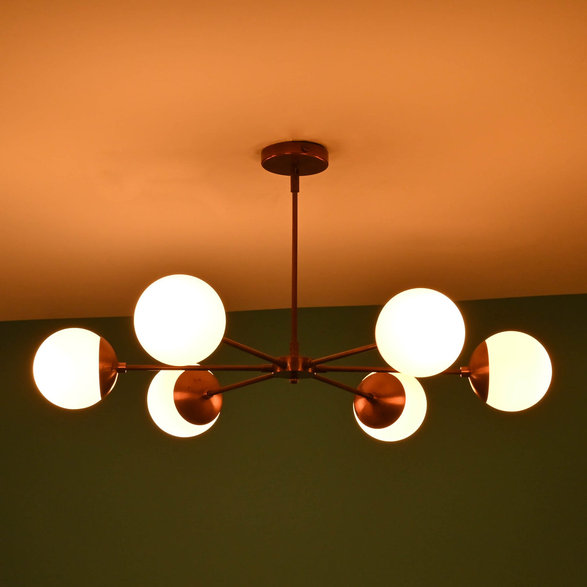 Angled night view of 6 light glass globe brass chandelier with glowing opal glass globes and elegant brass finish