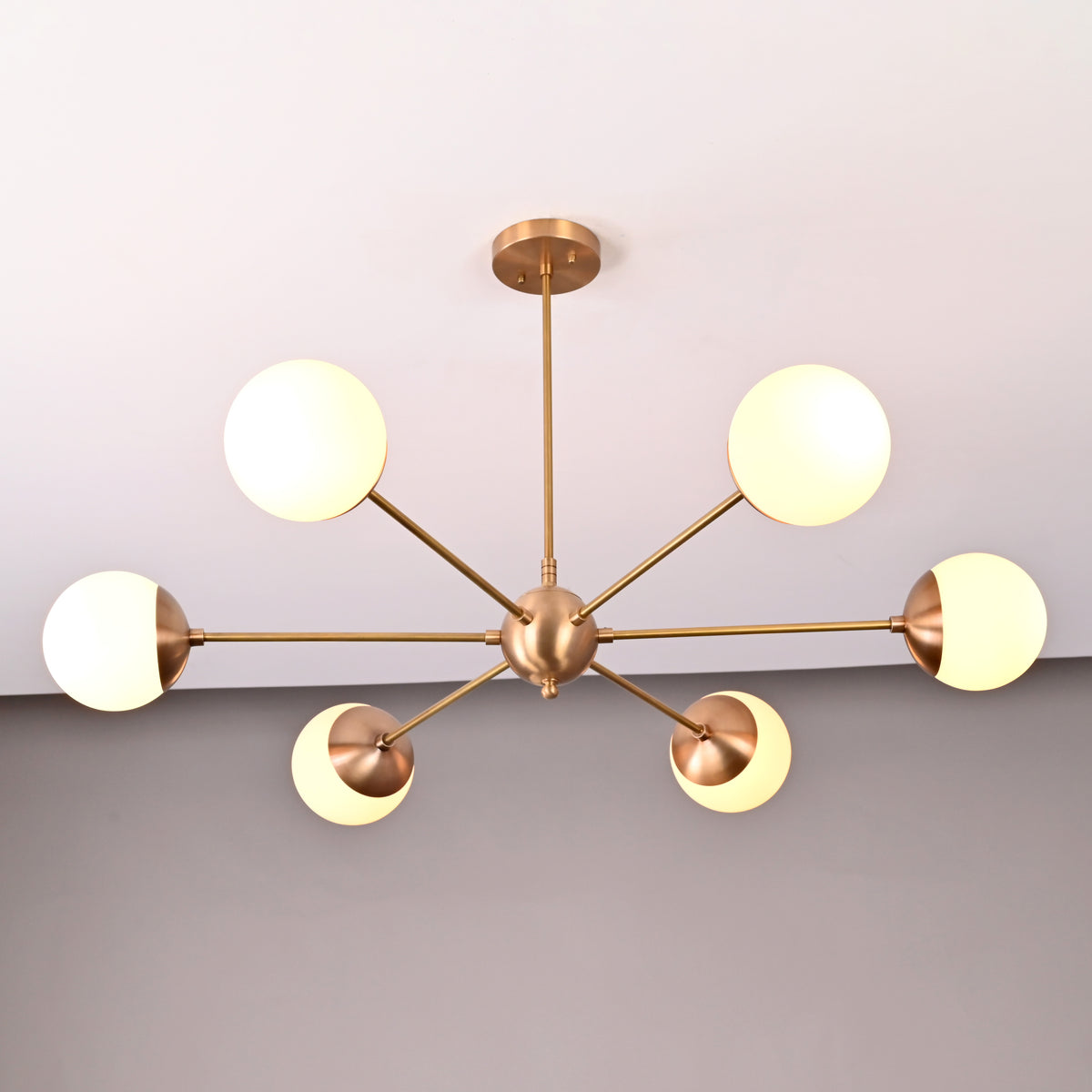 Mid-century style brass chandelier with six opal glass globes arranged symmetrically in a radial form.