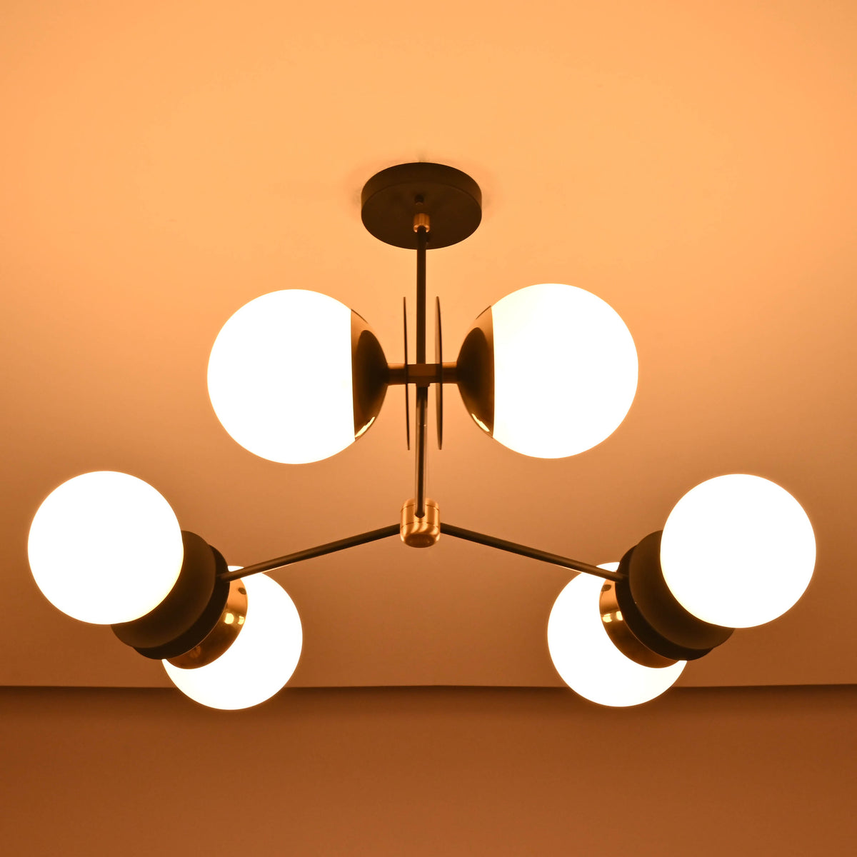 Evening view of a modern brass chandelier with opal glass globes casting soft indirect lighting.