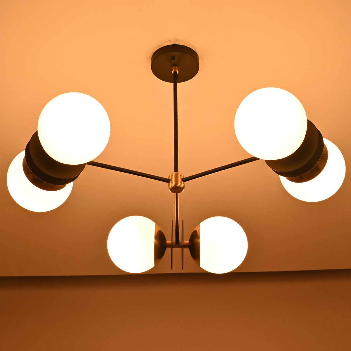 Warm-lit symmetrical view of a handcrafted opal glass globe brass chandelier suspended from the ceiling.