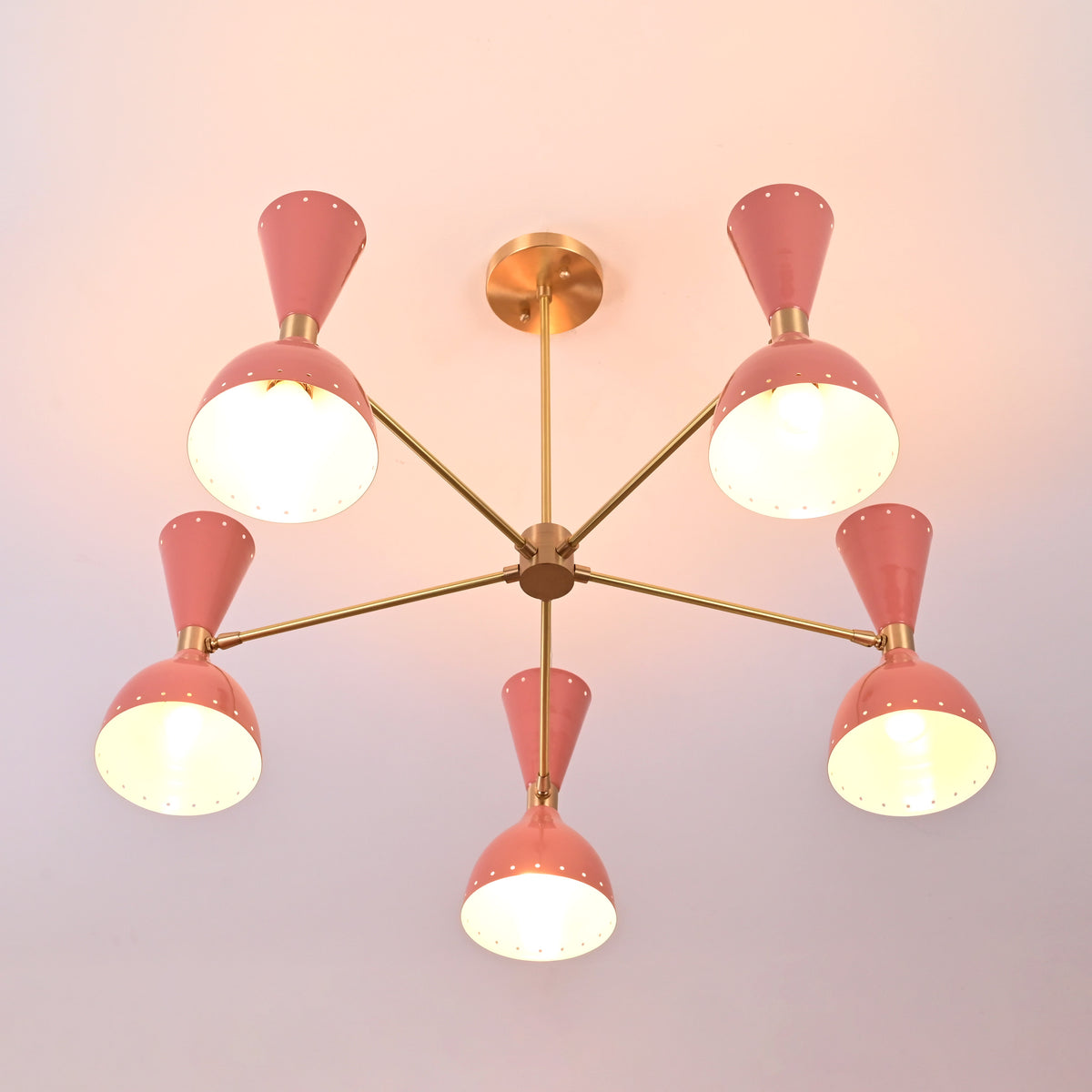 Bottom view of six-light peach brass chandelier with perforated shades emitting soft glow