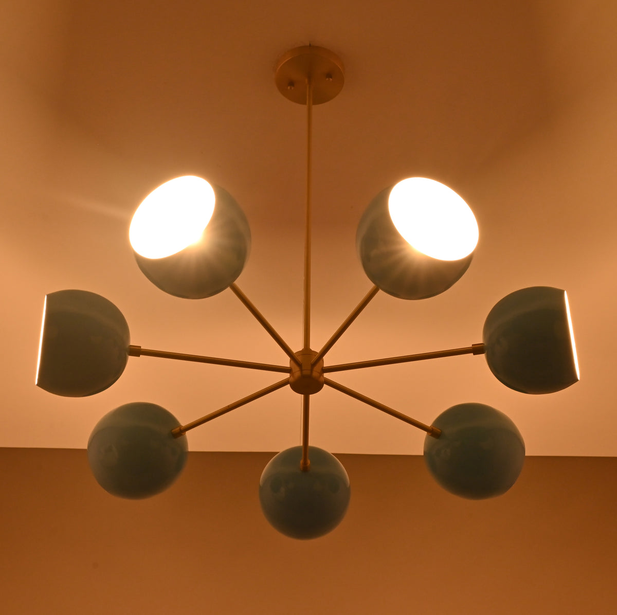 Installed 7 bowl brass chandelier emitting warm ambient light with blue glass shades