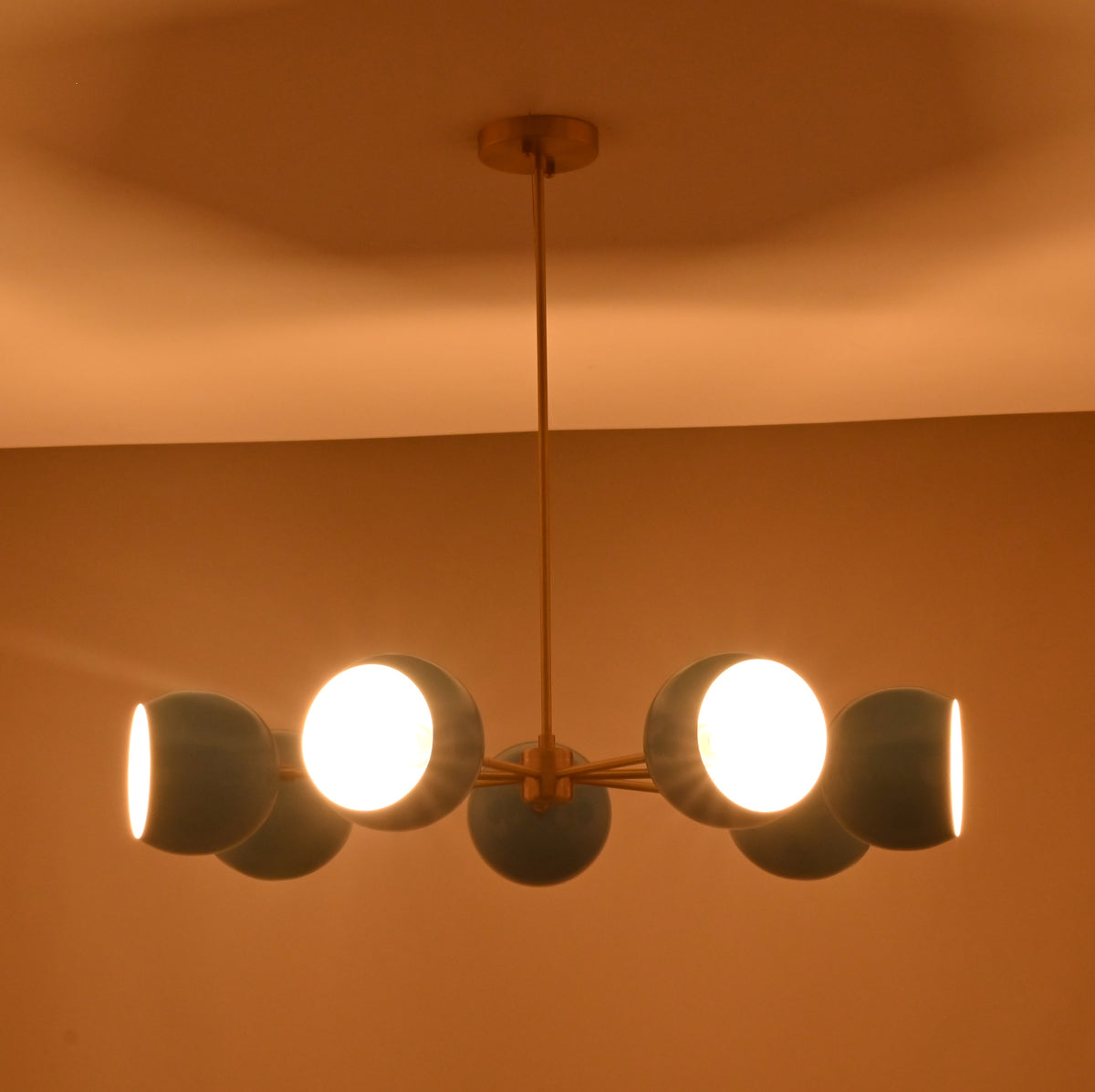 Symmetrical 7 bowl brass chandelier with blue glass shades installed in contemporary space