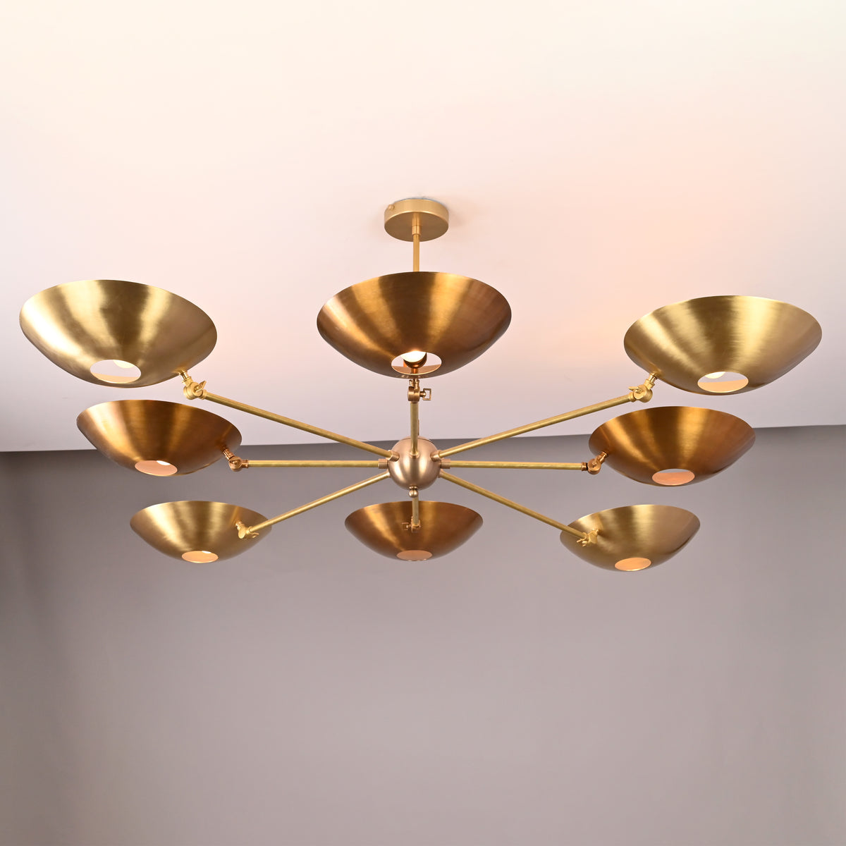 Large modern brass disc chandelier featuring eight adjustable arms and wide concave shades, ceiling mounted.