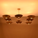 Evening-lit brass disc chandelier with eight disc shades emitting soft warm light in a symmetrical layout.