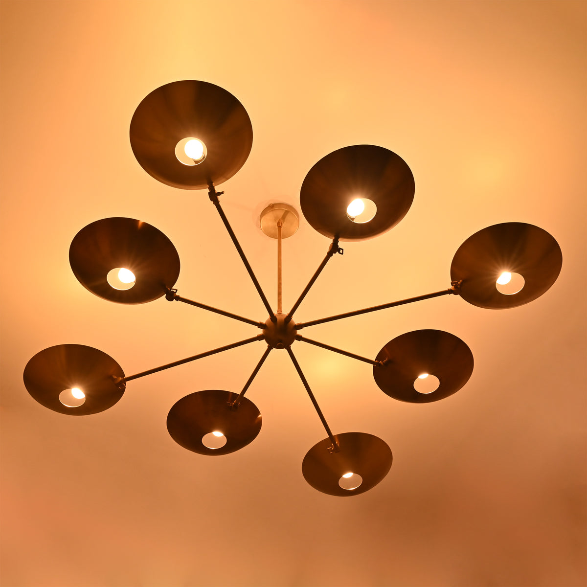 Warm-lit brass disc chandelier with eight glowing bulbs and circular concave brass shades.