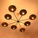 Warm-lit brass disc chandelier with eight glowing bulbs and circular concave brass shades.