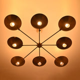 Illuminated 8-light brass chandelier viewed from below, featuring mid-century style disc shades.