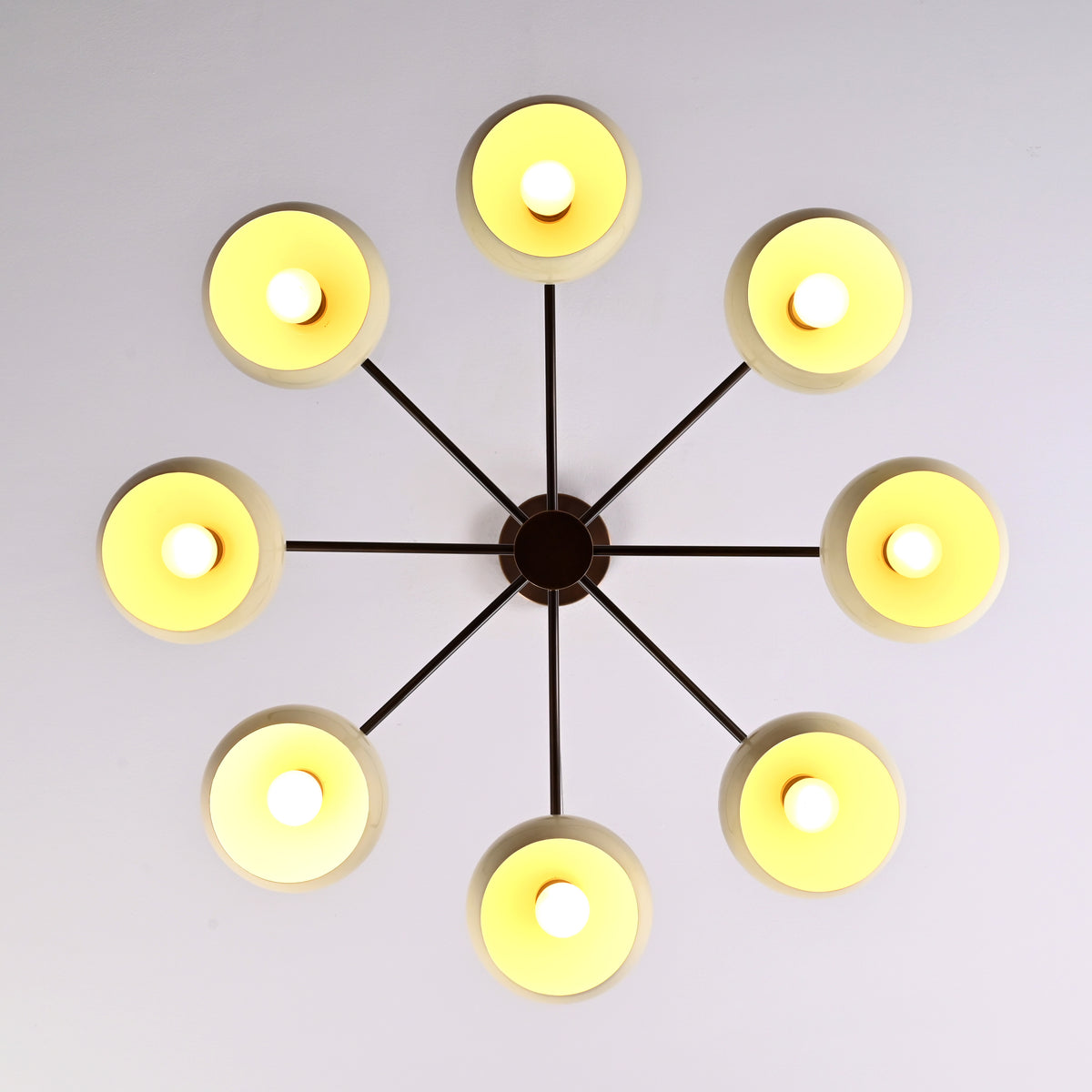 Top-down view of illuminated 8-light brass chandelier with evenly spaced bowl shades creating warm ambient glow.