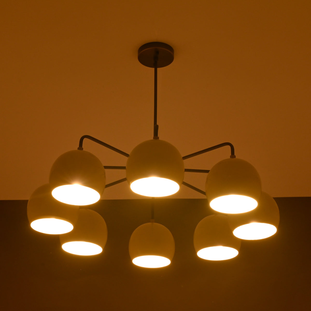 8-light brass chandelier glowing with warm ambient lighting, featuring dome-shaped shades and minimalist arms.