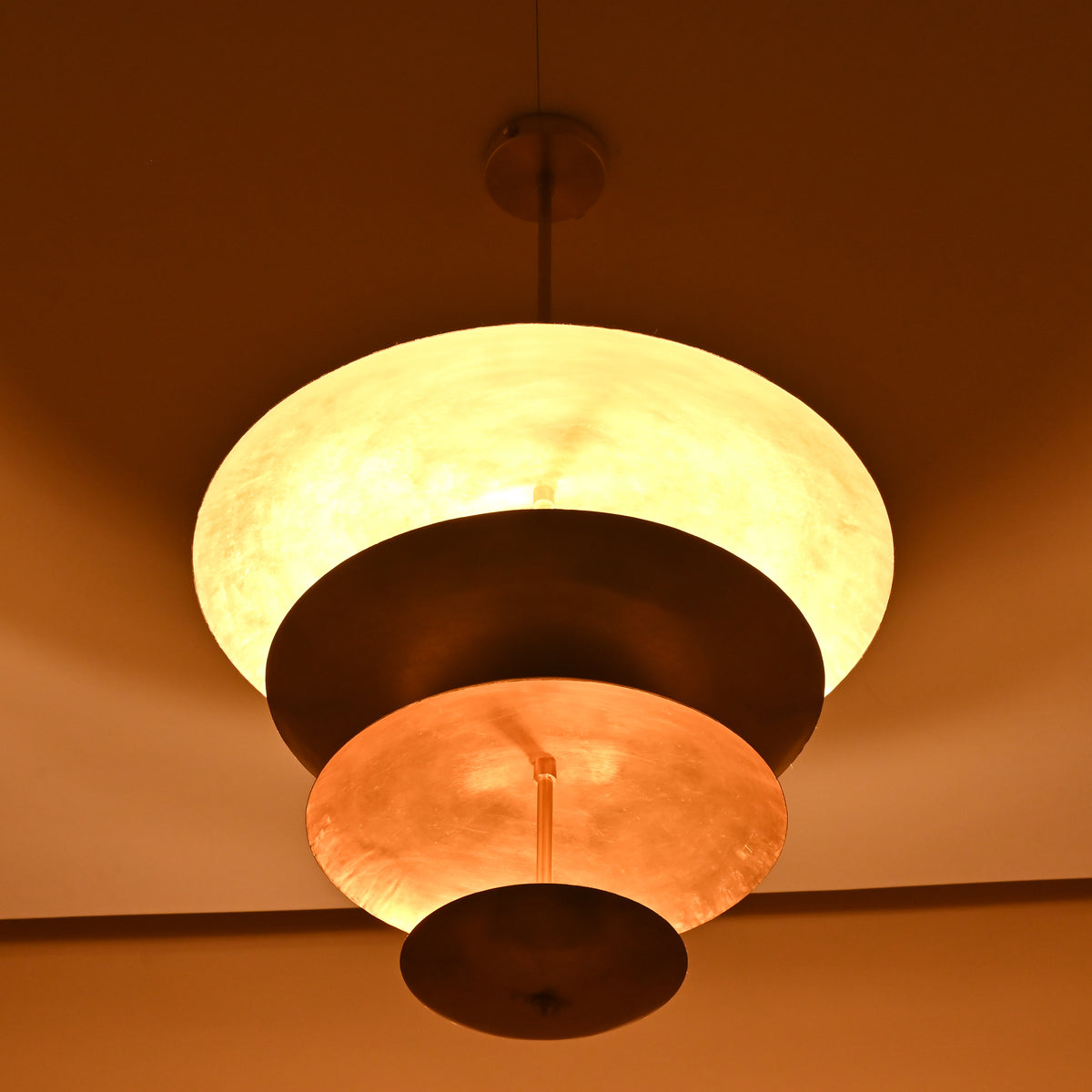 Elegant raw brass hanging light with tiered bowls creating soft ambient lighting