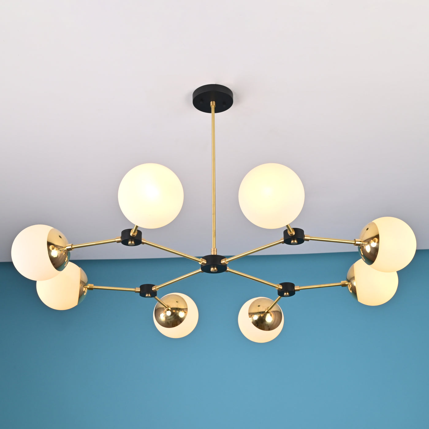 Front view of an 8-light brass globe linear sputnik chandelier with opal glass shades and black accents, suspended from the ceiling in a modern interior.