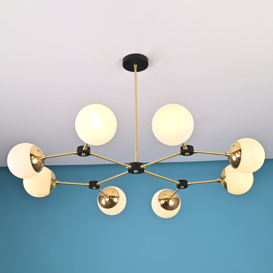 Front view of an 8-light brass globe linear sputnik chandelier with opal glass shades and black accents, suspended from the ceiling in a modern interior.