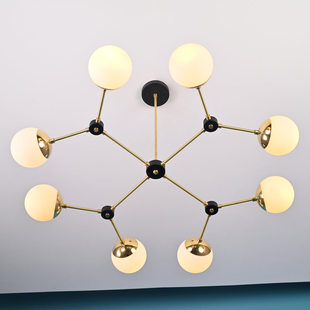 Angled view of an 8-light brass linear chandelier with opal globe shades and black joint details, highlighting its balanced modern design.