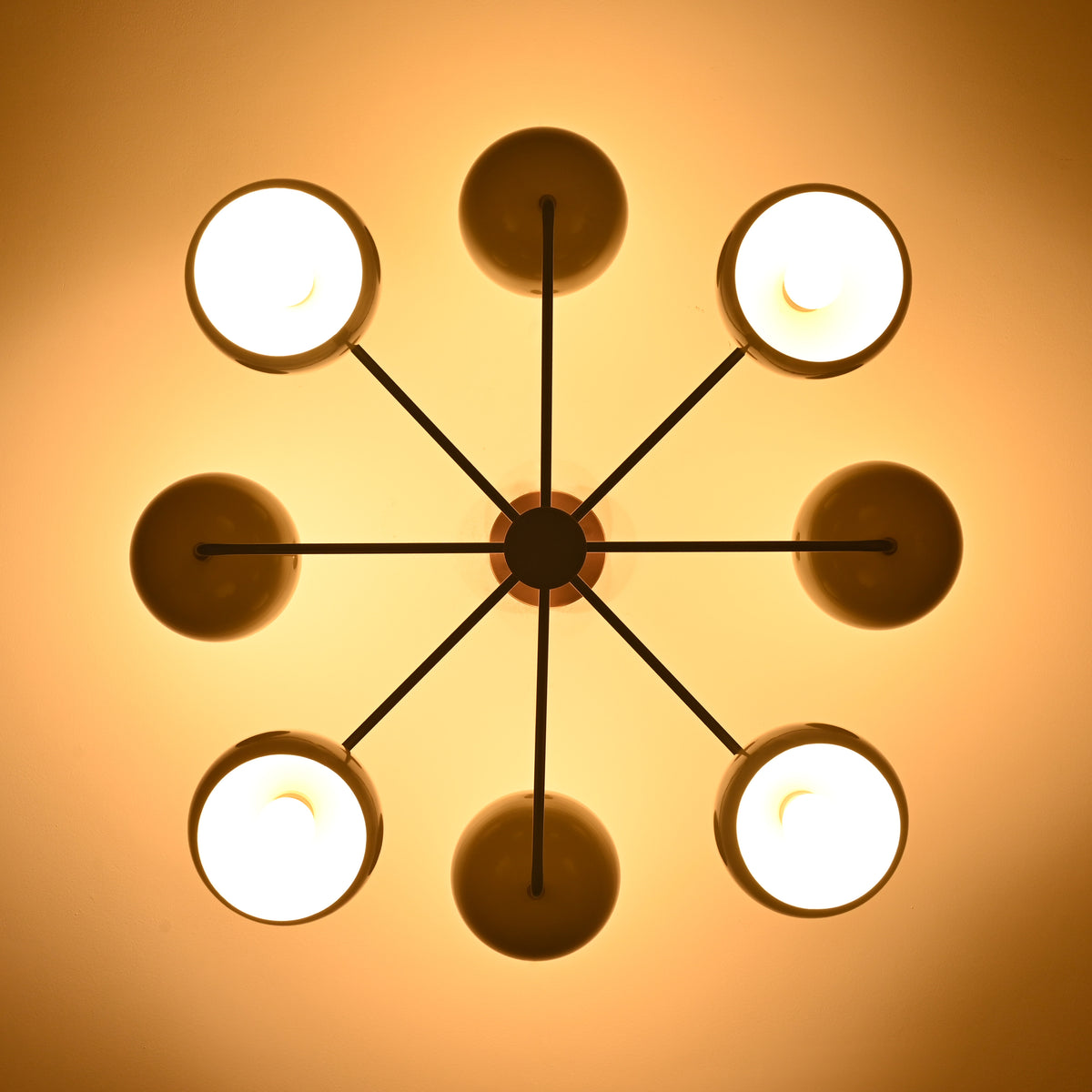 Warm top-view photo of 8-light brass chandelier casting soft, diffused lighting through bowl-shaped shades.
