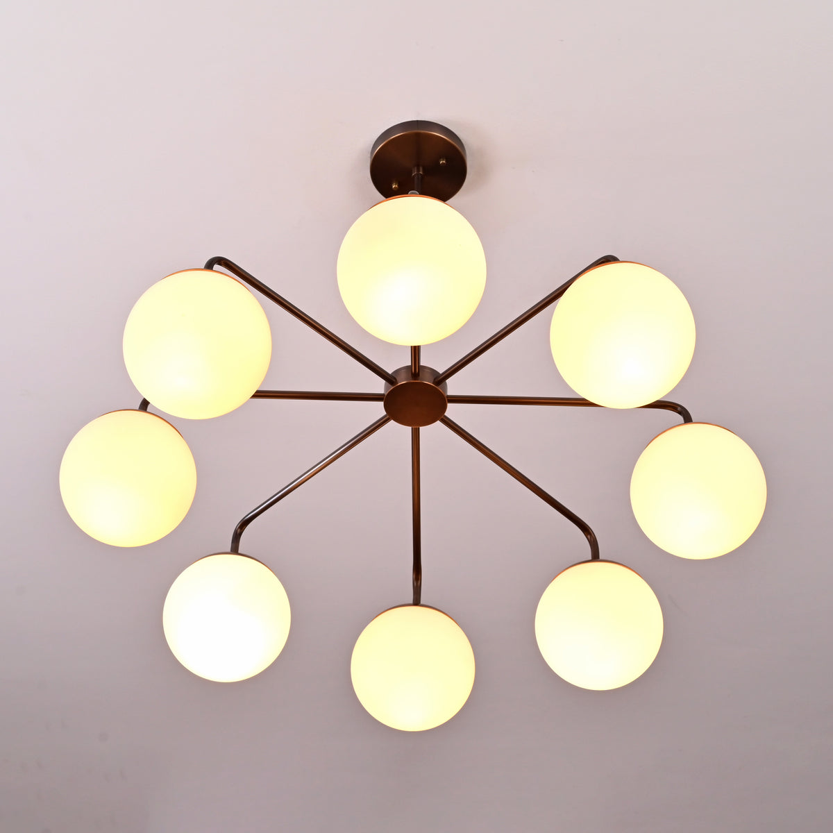 Mid-century style brass chandelier featuring eight glowing opal globes arranged in a sculptural radial design.