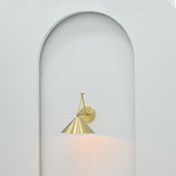 Adelaide brass cone wall sconce mounted inside a minimalist white arched wall niche with elegant round backplate and downward-facing metal shade.