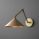 Adjustable brass swing arm wall sconce with cone shade and round backplate, modern industrial wall lamp on gray wall.