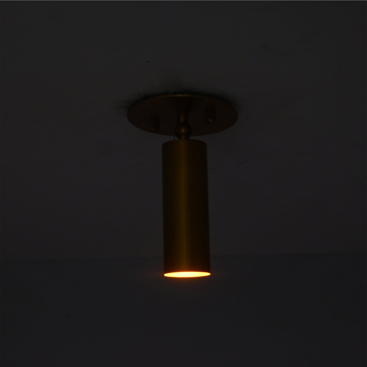 Lit view of Alden adjustable brass ceiling spotlight casting a warm focused downward beam