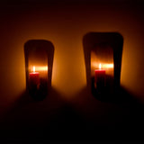 Front view of two Alden modern brass wall candle sconces with illuminated pillar candles casting a warm glow against a neutral wall.