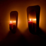 Angled view of handcrafted Alden brass wall candle sconces displaying lit pillar candles with elegant architectural backplates and warm candlelight.