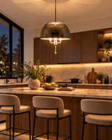 Alexandria reflective chrome dome pendant hanging above a marble kitchen island with upholstered counter stools, walnut cabinetry, and warm ambient lighting in a sophisticated contemporary kitchen.