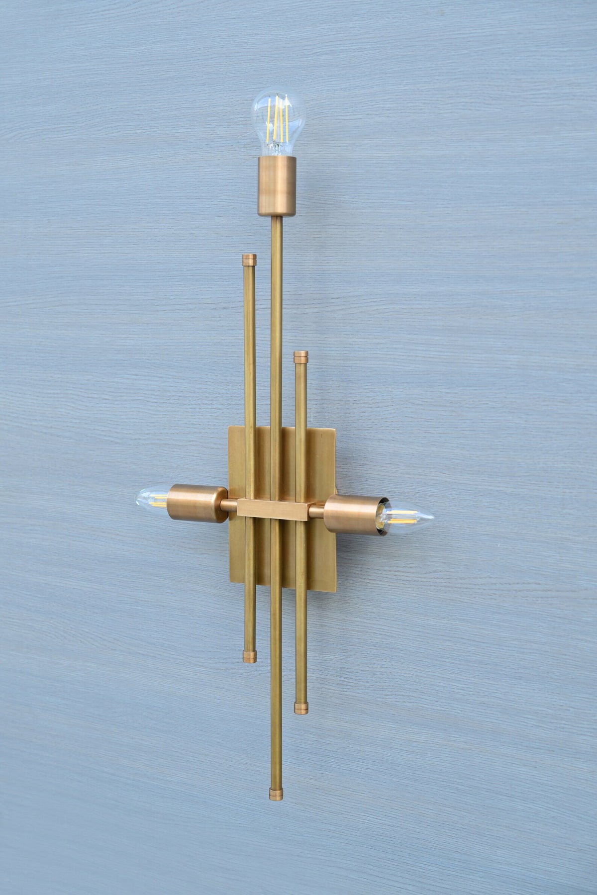 Angled photo of brass wall sconce showing vertical rods and three bulb holders, designed for contemporary interiors.