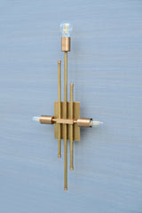Angled photo of brass wall sconce showing vertical rods and three bulb holders, designed for contemporary interiors.