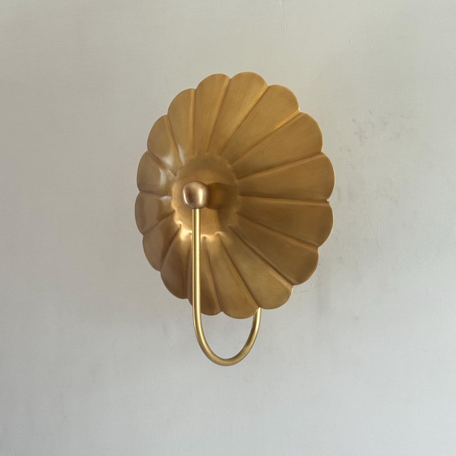 Front view of brass flower wall sconce with scalloped disc backplate and curved stem in brushed brass finish.