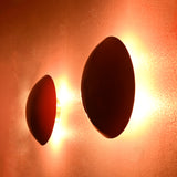 Side angled view of two glowing red disc wall sconces with warm radiant brass halo lighting effect