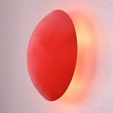 Angled side view of handmade red circular wall sconce, glowing softly with indirect ambient light