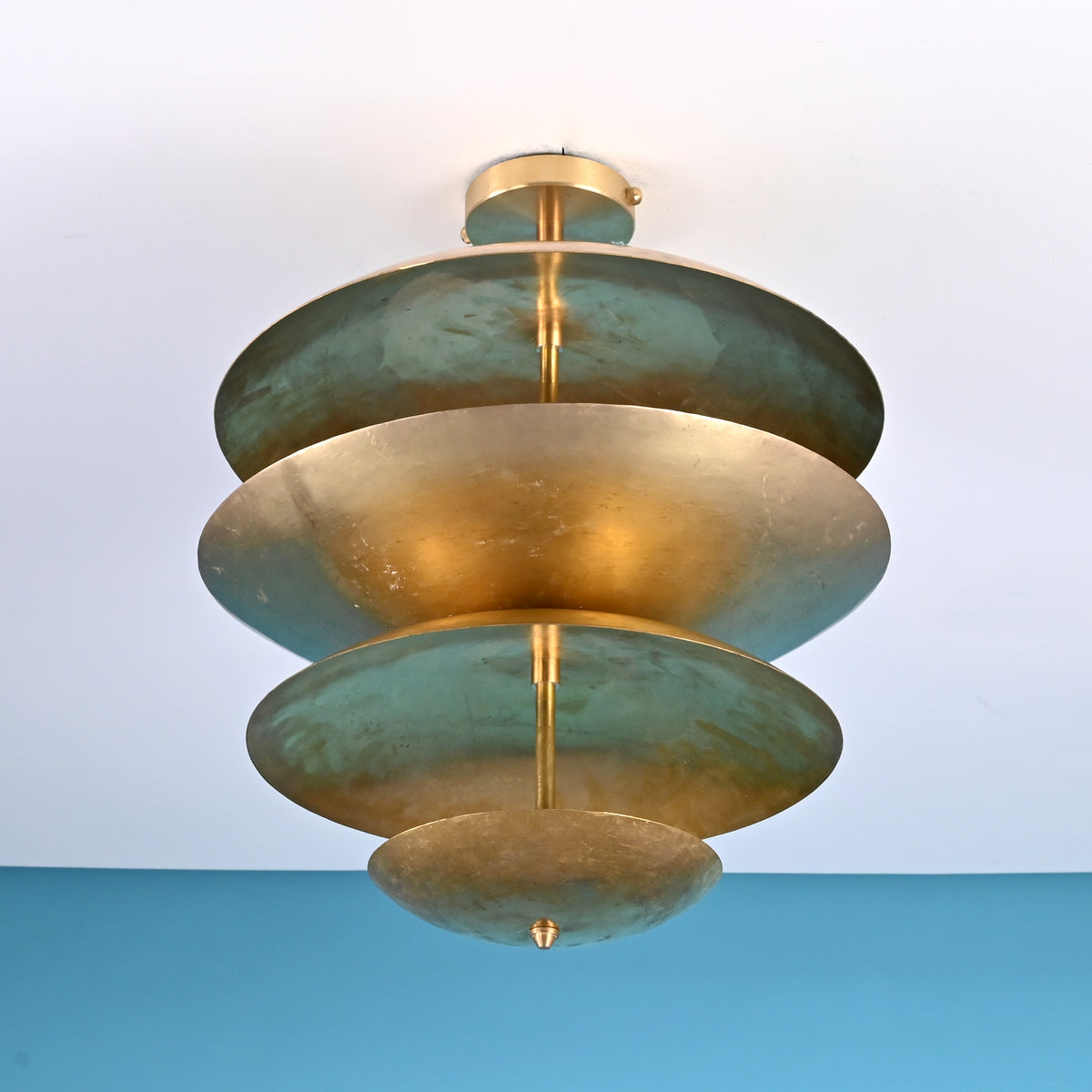 Angled view of custom brass disc flushmount ceiling light with five tiered shades in brushed brass and green oxidized patina