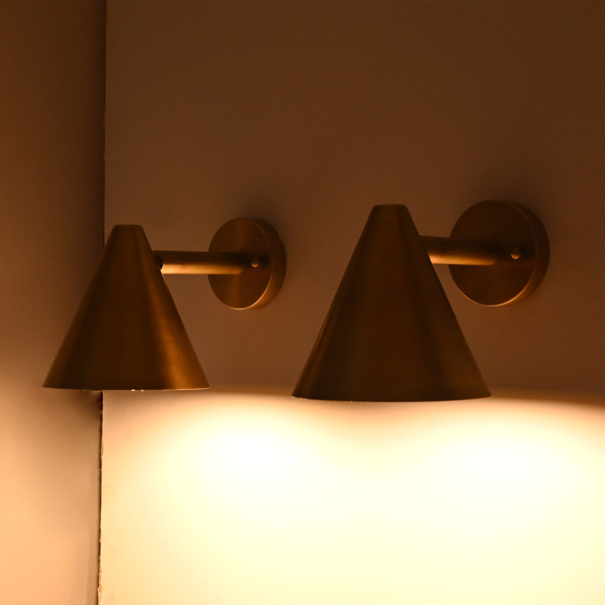 Pair of Aria tapered cone brass wall sconces installed on a corner wall creating soft downward architectural lighting.