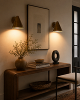 Pair of Aria modern tapered cone brass wall sconces installed in a contemporary entryway above a wooden console, providing warm ambient illumination.