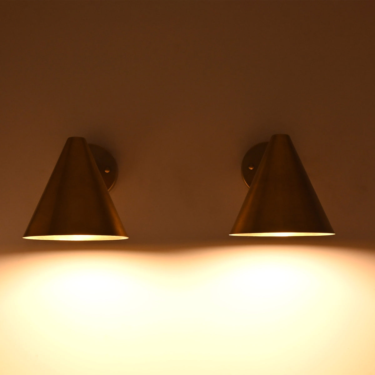 Pair of Aria tapered cone brass wall sconces displaying balanced warm ambient lighting on a wall.