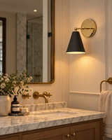 Aspen matte black and polished brass wall sconce illuminating a luxurious bathroom vanity with marble countertop, brass fixtures, wooden cabinetry, and framed mirror.
