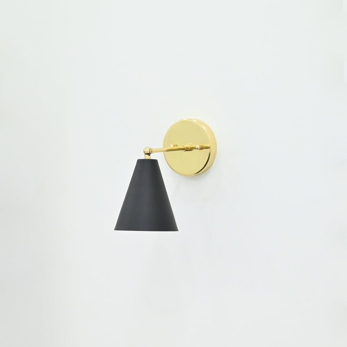 Aspen 1-light wall sconce featuring a matte black tapered cone shade, polished brass horizontal arm, and round gold backplate mounted on a white wall.