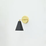 Aspen 1-light wall sconce featuring a matte black tapered cone shade, polished brass horizontal arm, and round gold backplate mounted on a white wall.