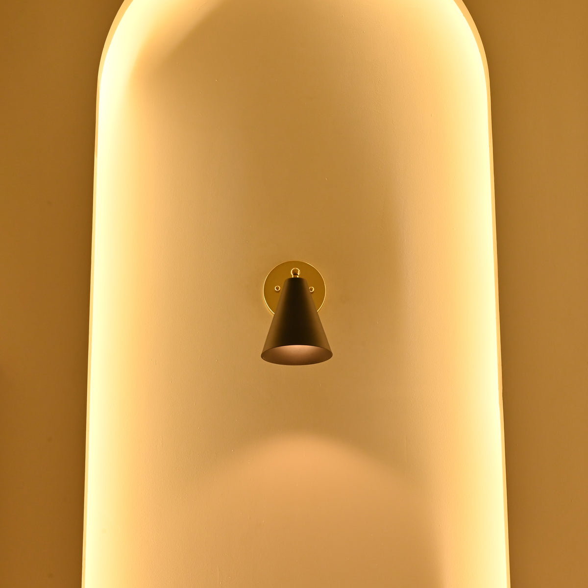 Aspen black tapered cone wall sconce displayed in a tall arched niche surrounded by warm golden ambient lighting.