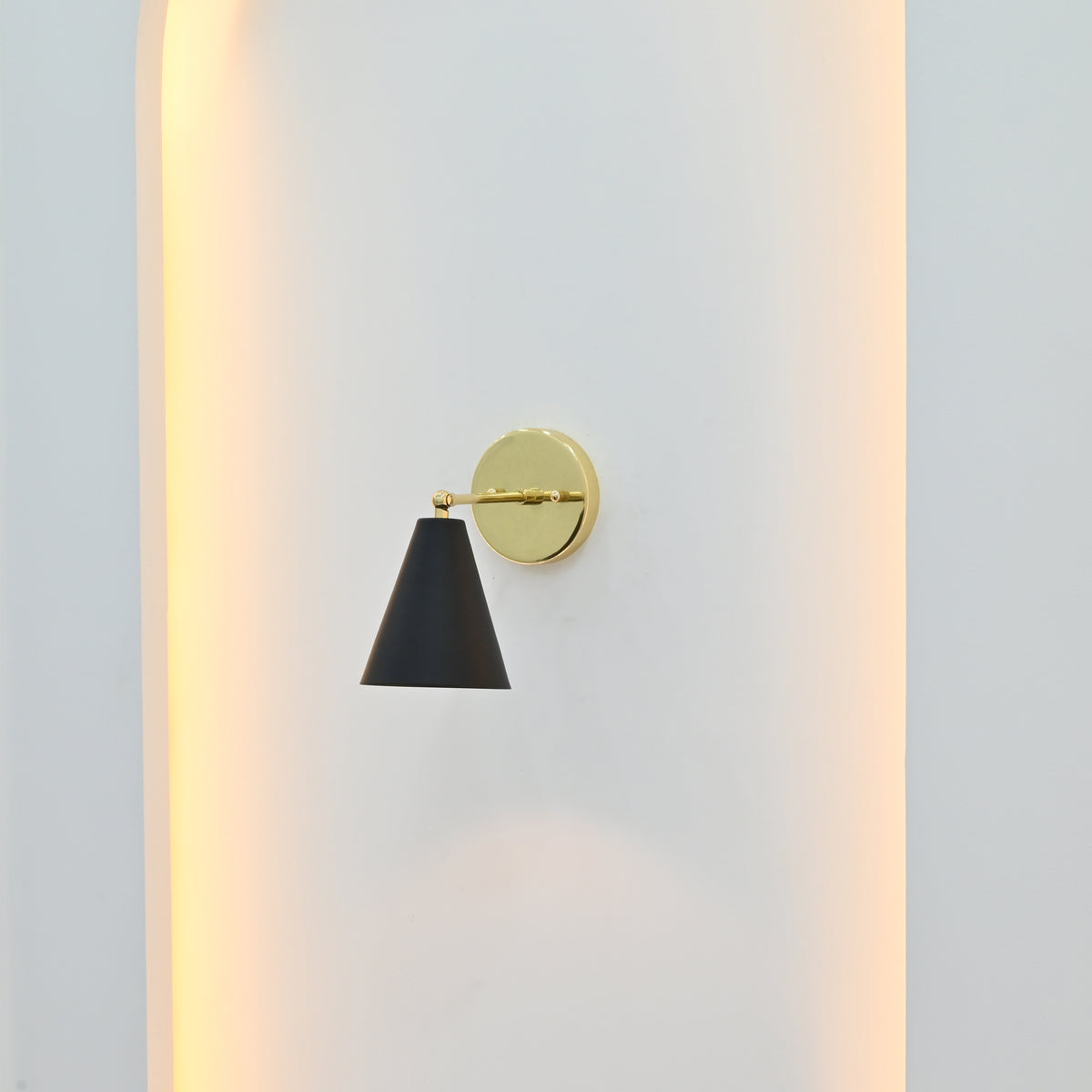 Aspen Mid-Century Modern black and brass wall sconce mounted inside a white architectural wall niche with soft warm ambient lighting.