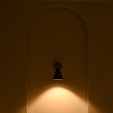 Aspen modern black cone wall sconce casting focused warm downward illumination onto a recessed wall niche in a dark interior.