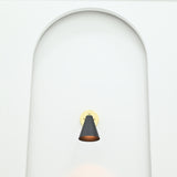 Front view of Aspen single-light black cone wall sconce with circular polished brass backplate installed inside a minimalist white arched wall niche.