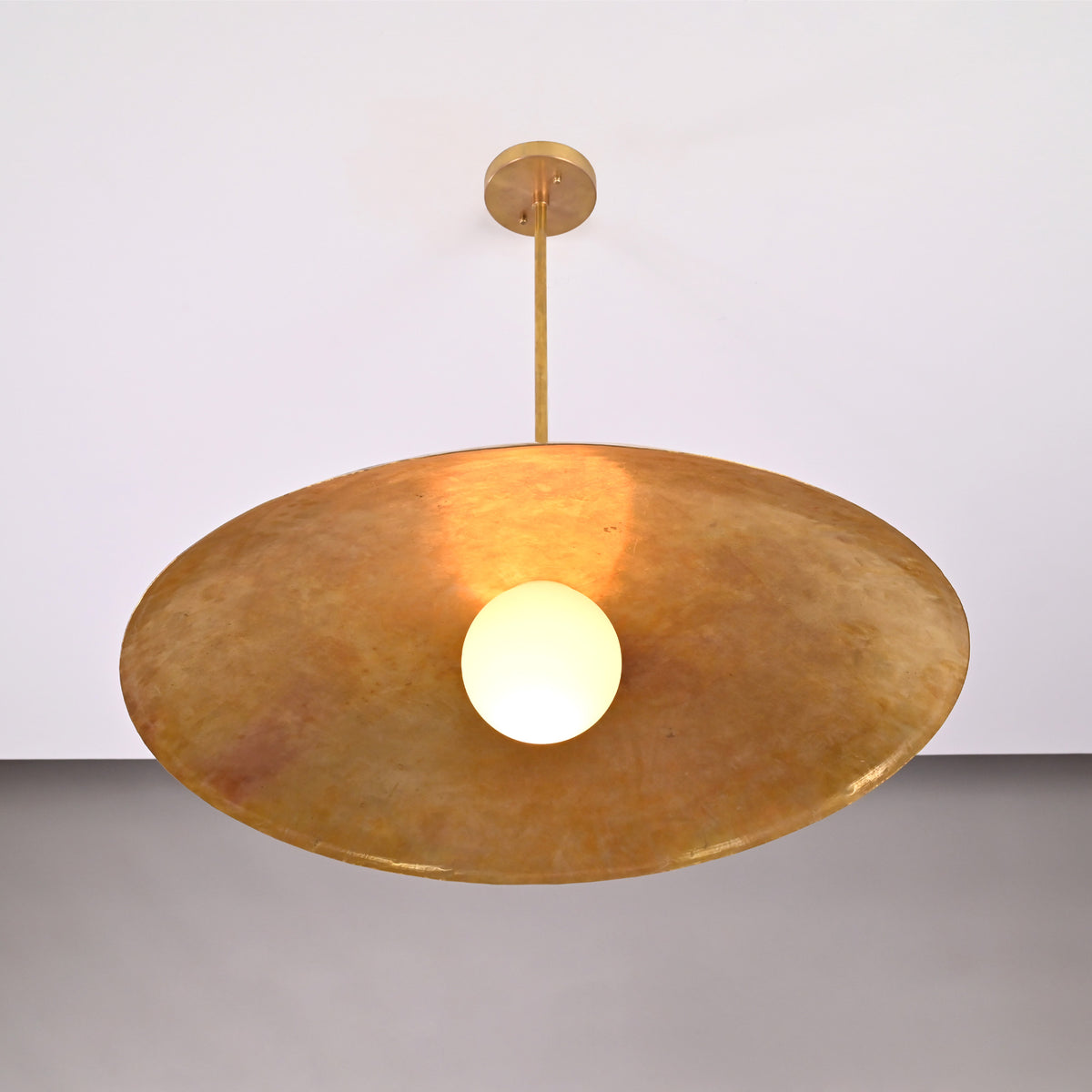 Close up of Aurelia Globe Saucer Pendant Light with warm globe illumination beneath the wide shade.