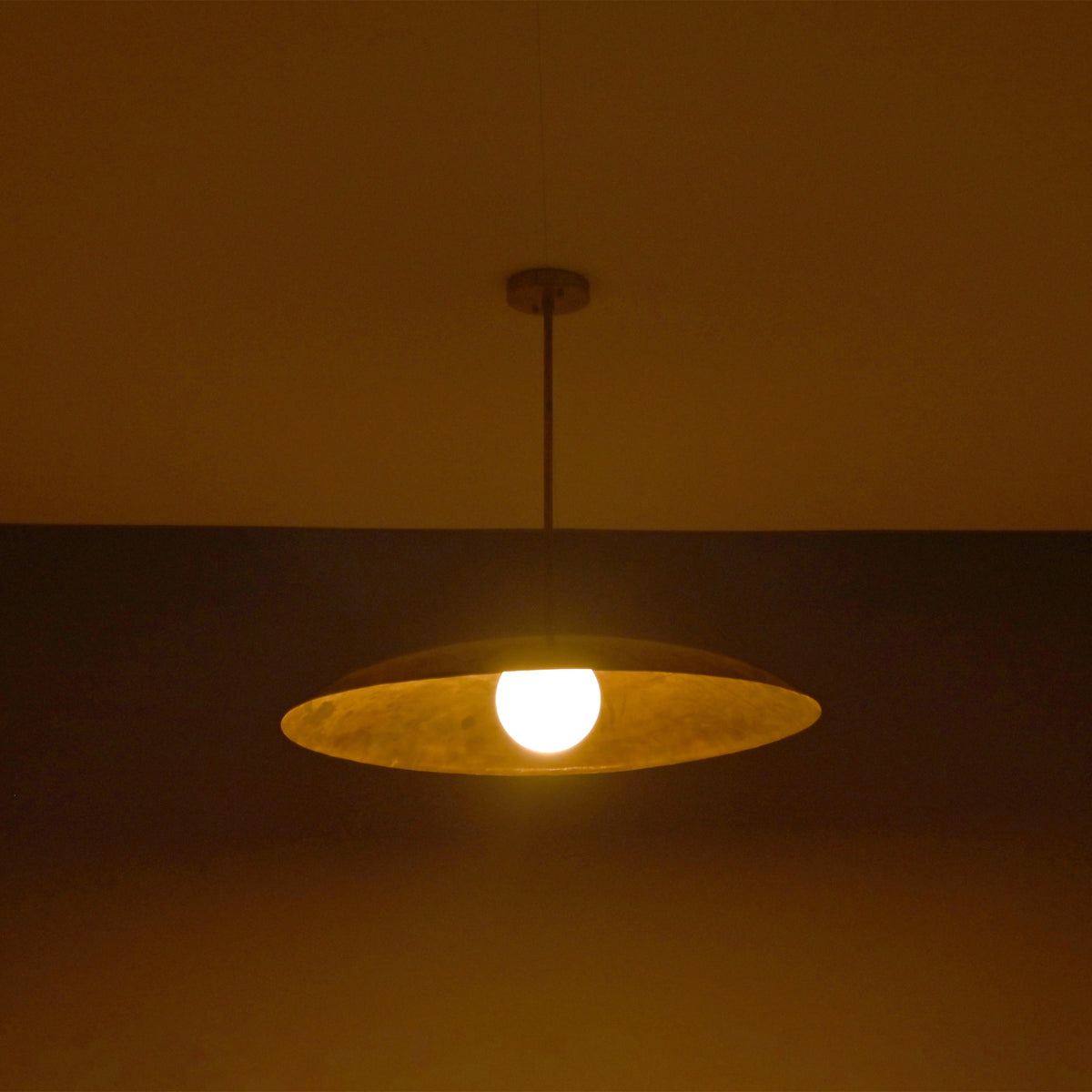 Wide evening view of Aurelia Globe Saucer Pendant Light highlighting the warm globe bulb and dome profile.