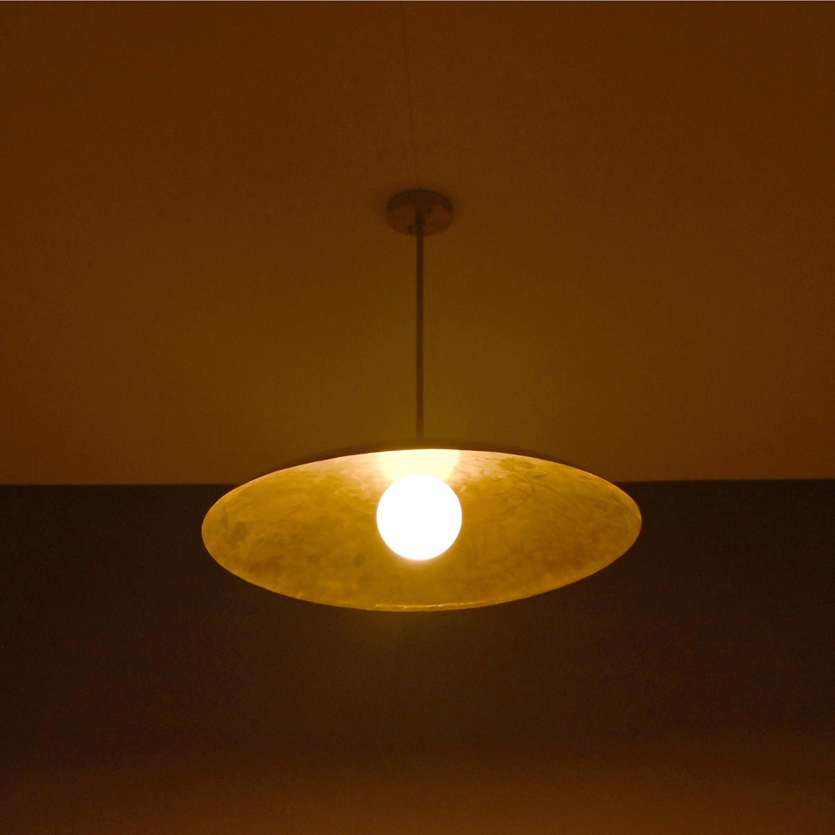 Aurelia Globe Saucer Pendant Light glowing in a dark setting with soft warm ambient lighting effect.
