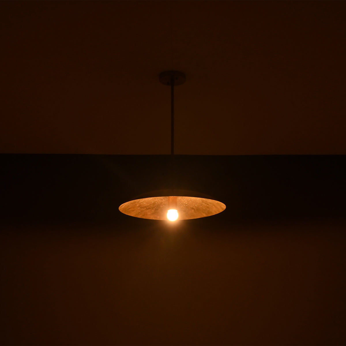 Wide view of Aurelia Petite Saucer Pendant Light illuminated in low light with soft ambient glow.